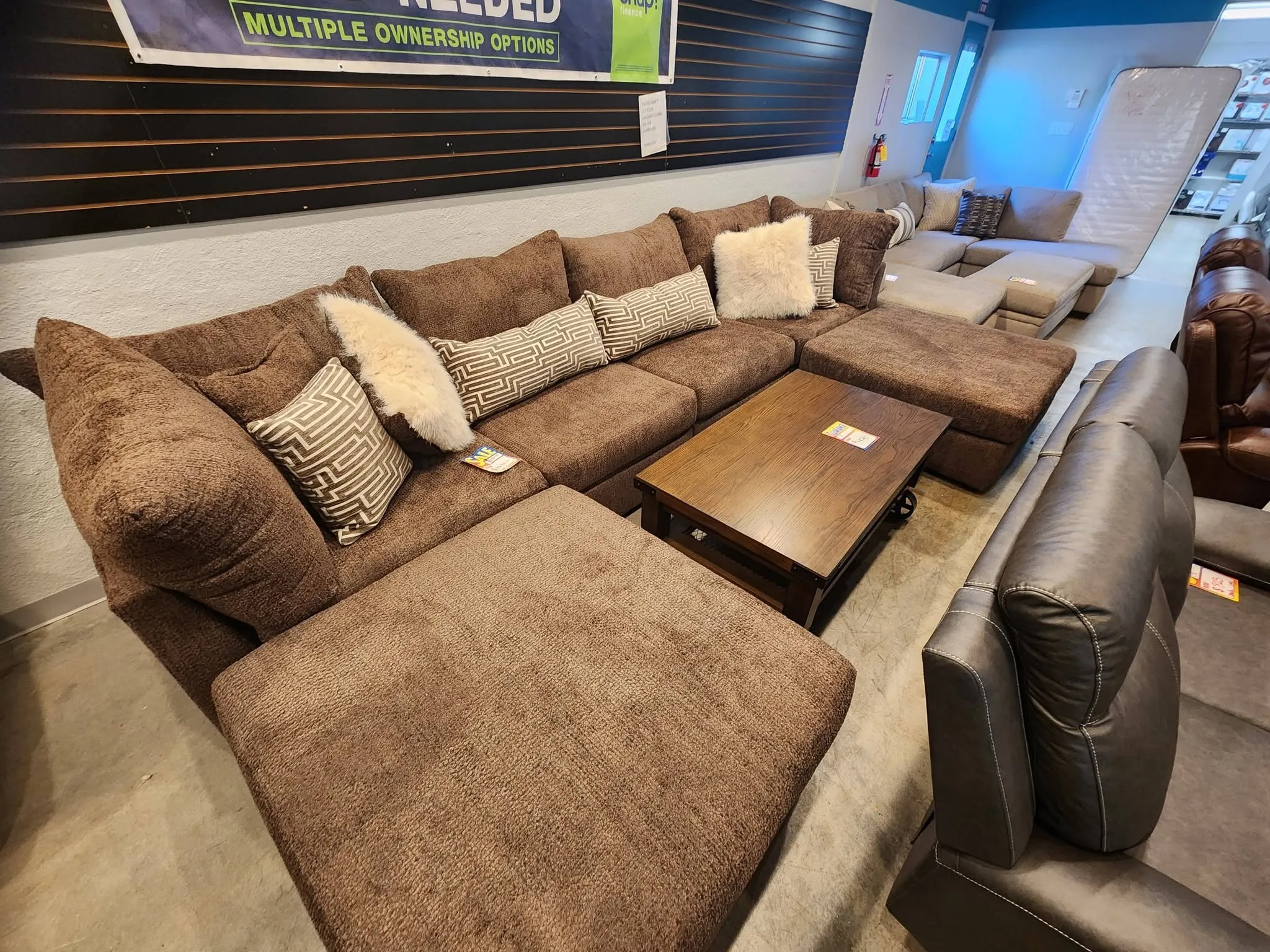 A large brown fabric sectional with ottomans and accent pillows on the BoxDrop Grass Valley floor